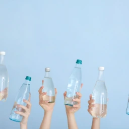 hands holding clear glass bottles over a clear blue sky